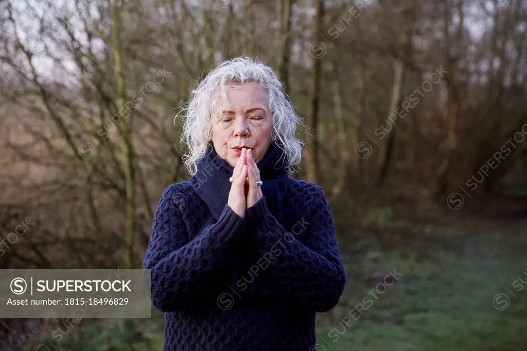 Senior woman with hands clasped standing in front of bare trees