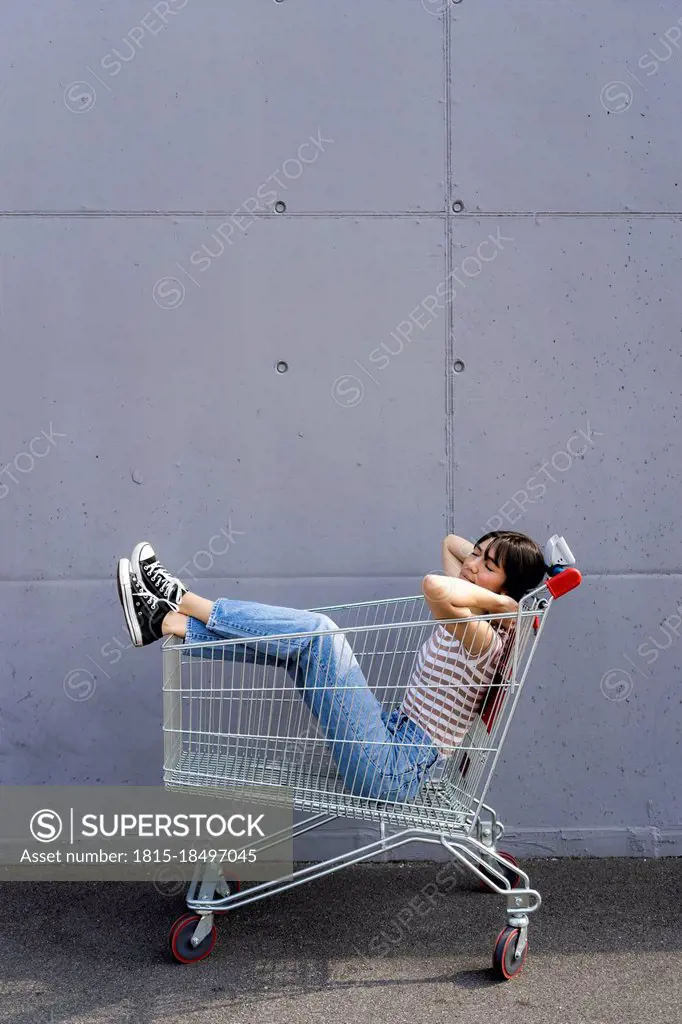 Woman sleeping in shopping cart on footpath