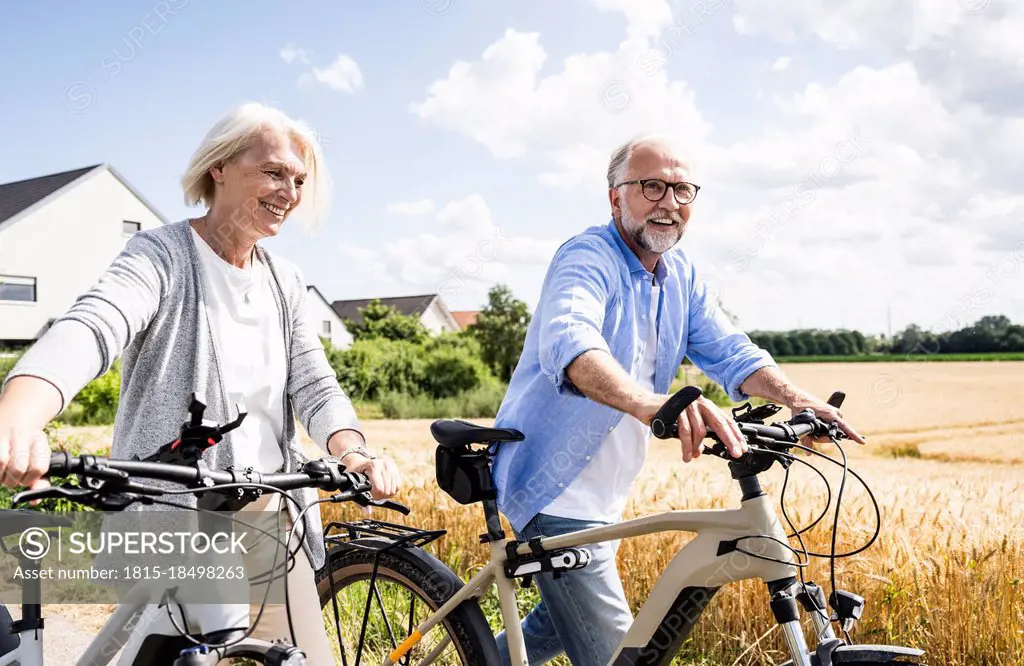 Smiling couple walking with bicycles during sunny day