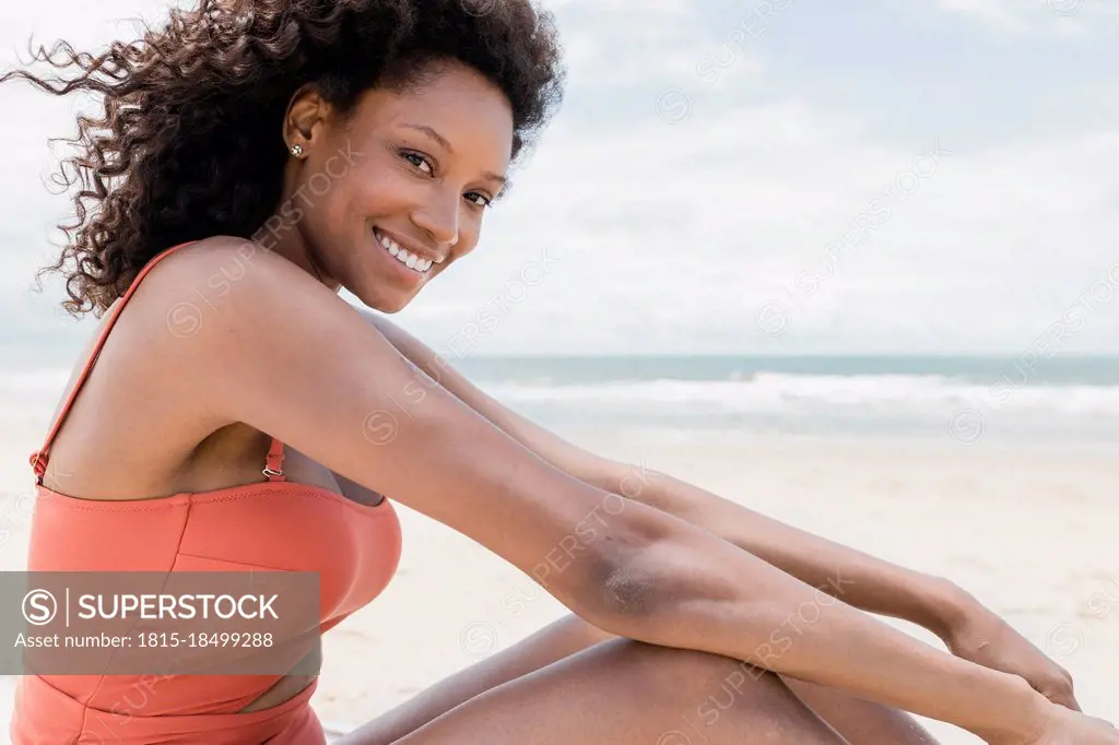 Happy young woman in swimsuit sitting at beach