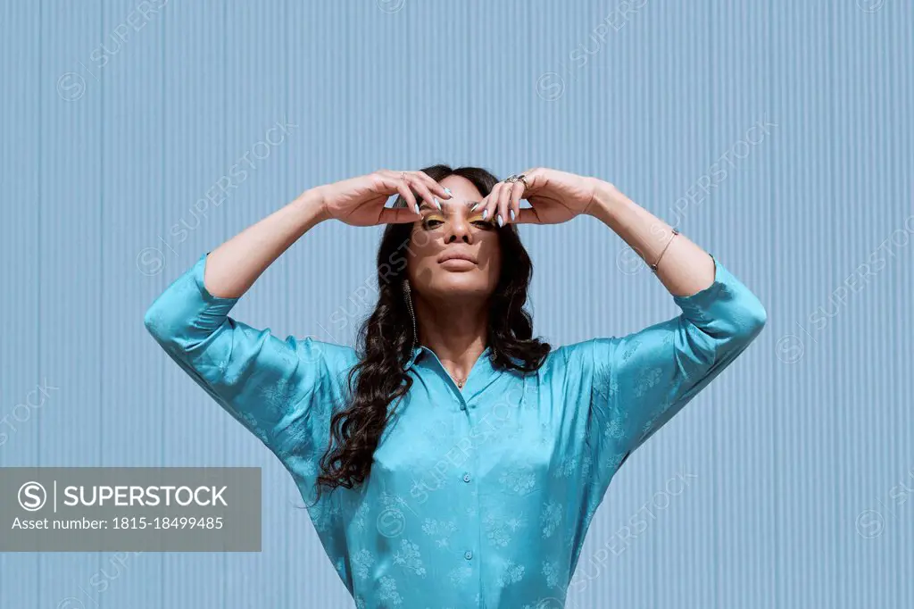 Woman standing with hands raised in front of blue wall