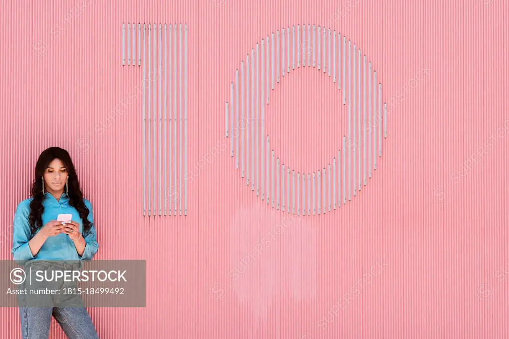 Female transgender using mobile phone by number 10 on pink corrugated wall