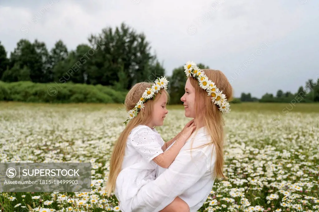 Smiling mother carrying daughter at chamomile field