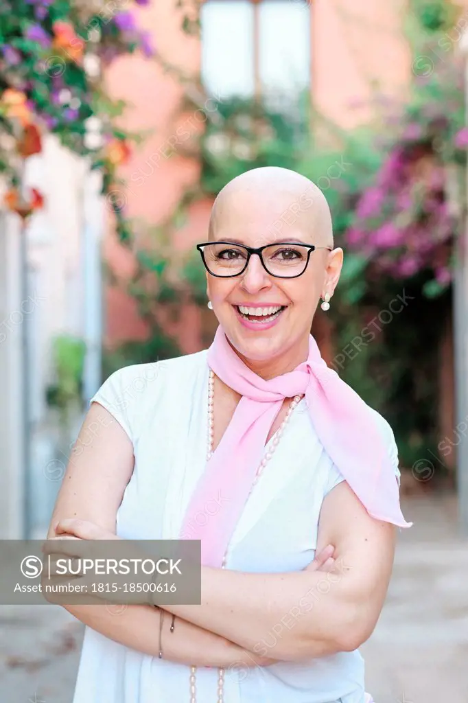 Happy mature woman with arms crossed standing at backyard