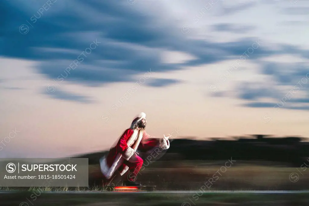 Man skateboarding on road wearing Santa Claus costume at dusk