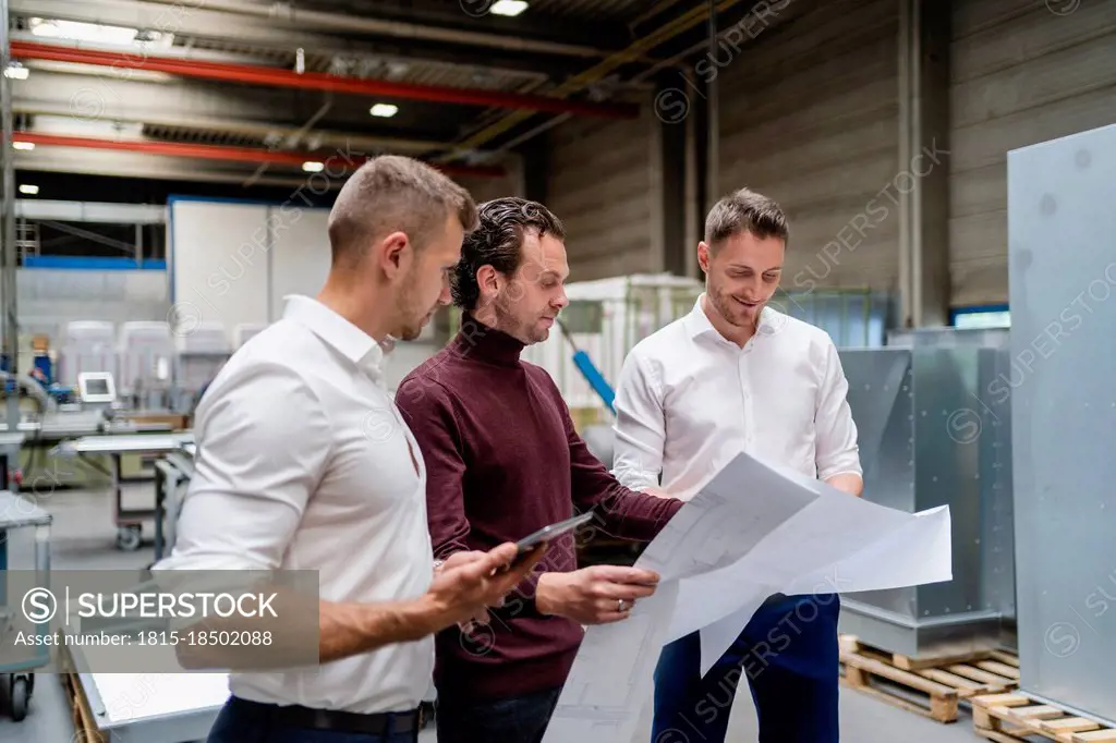 Male engineers checking blueprint at industry