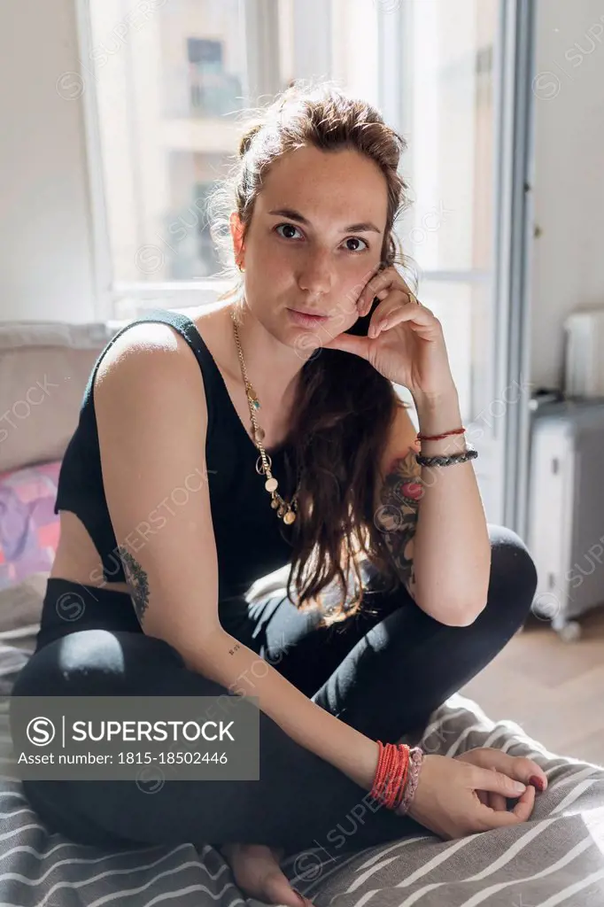 Woman staring while sitting cross-legged on bed in apartment