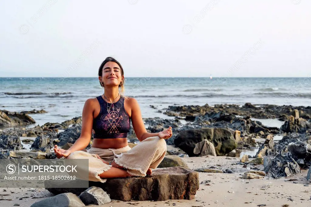 Smiling woman meditating on rock at beach