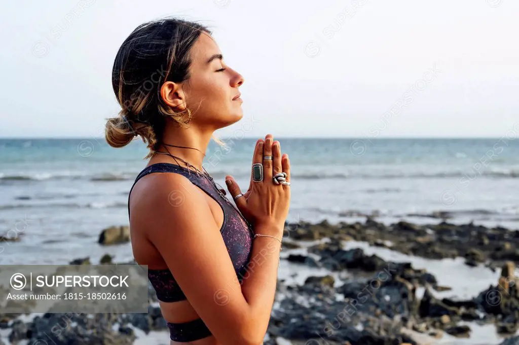 Young woman with hands clasped meditating at beach