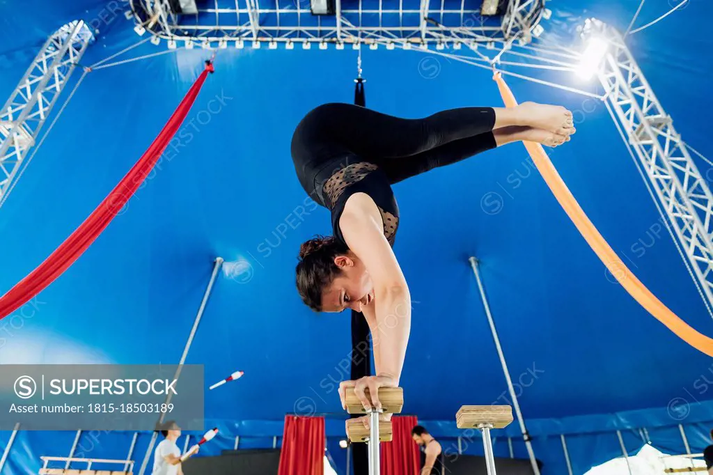 Female acrobat doing rehearsal on handstand cane with athletes in background