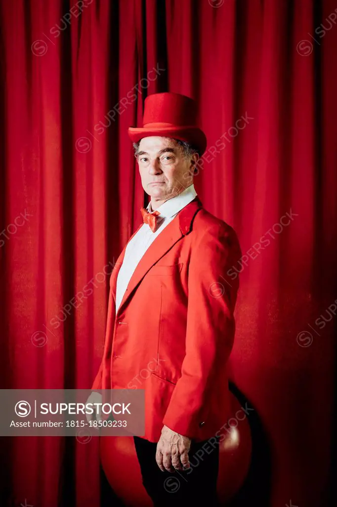 Male artist wearing hat standing by stage curtain