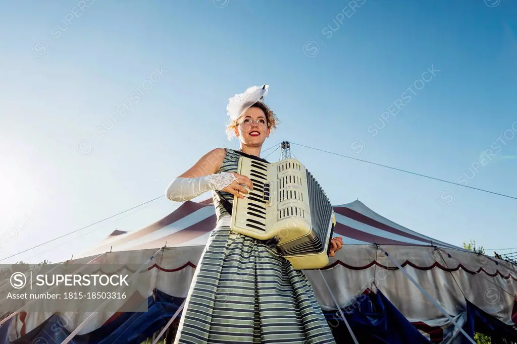 Female performer playing accordion in front of circus tent