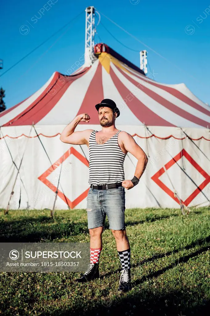 Male artist flexing muscle while standing on meadow