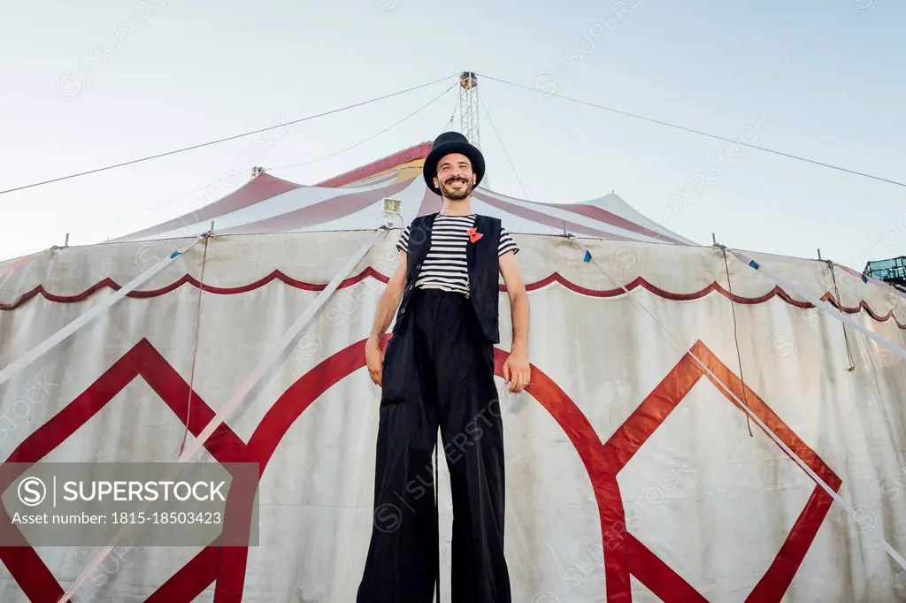 Male artist standing with stilts in front of circus tent