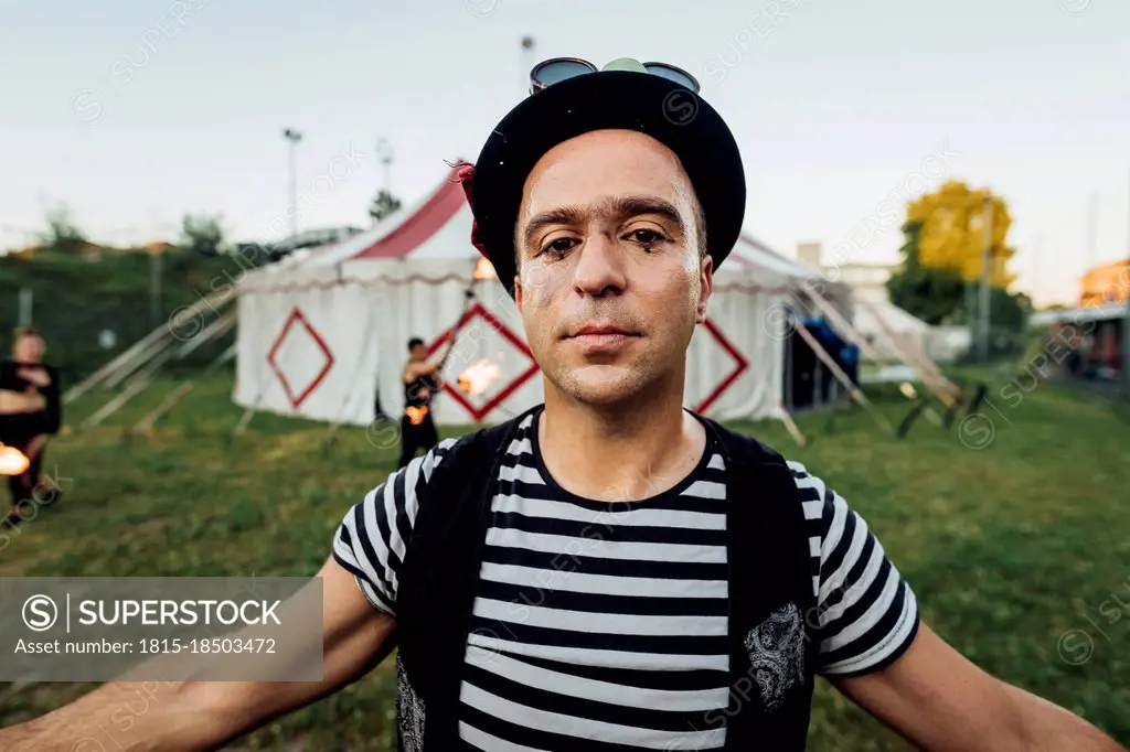 Male acrobat with arms outstretched standing outside circus tent