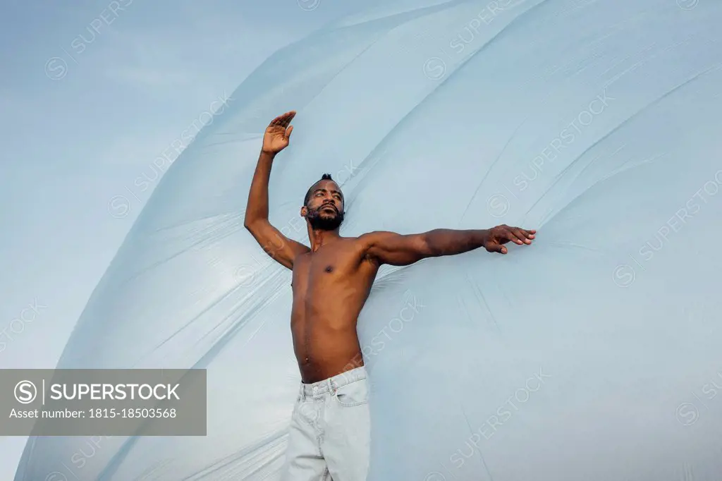 Shirtless man looking away while dancing in front of foil