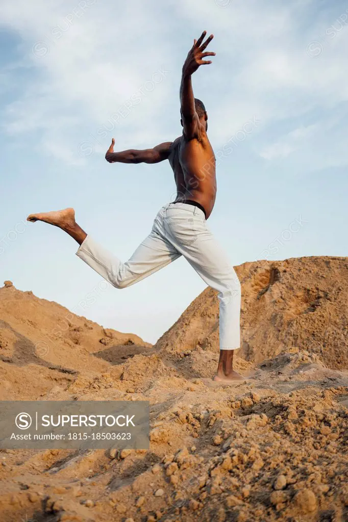 Shirtless man with arms outstretched dancing on sand