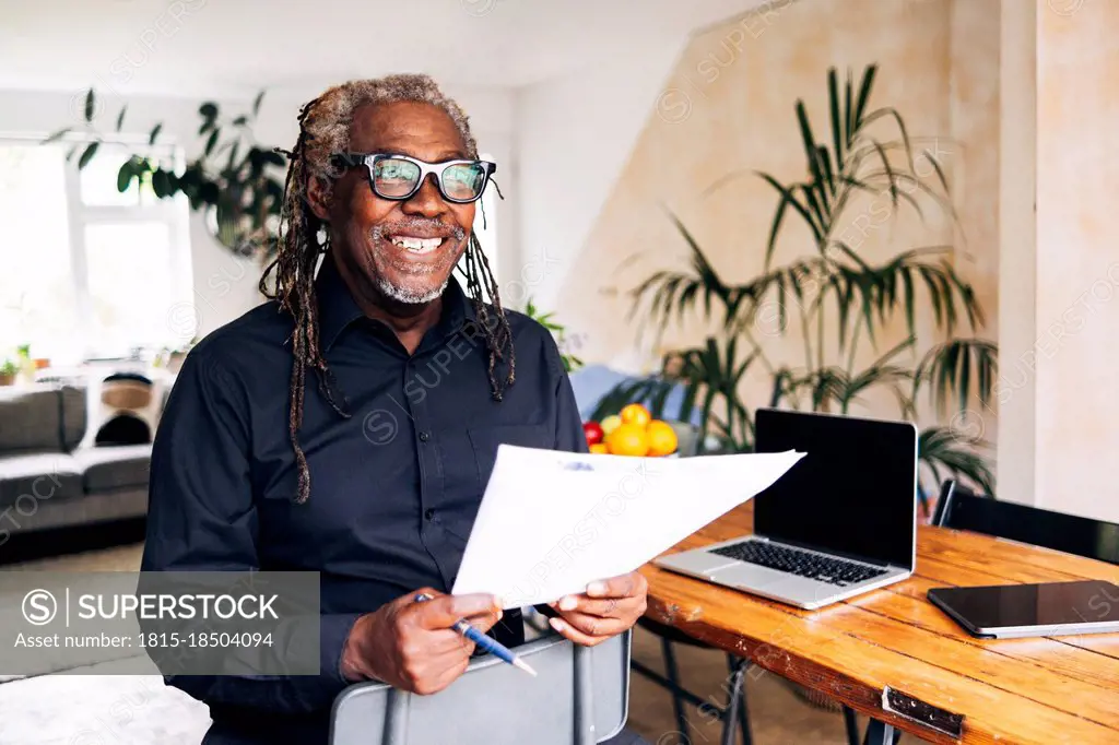 Smiling businessman holding document at desk in home office