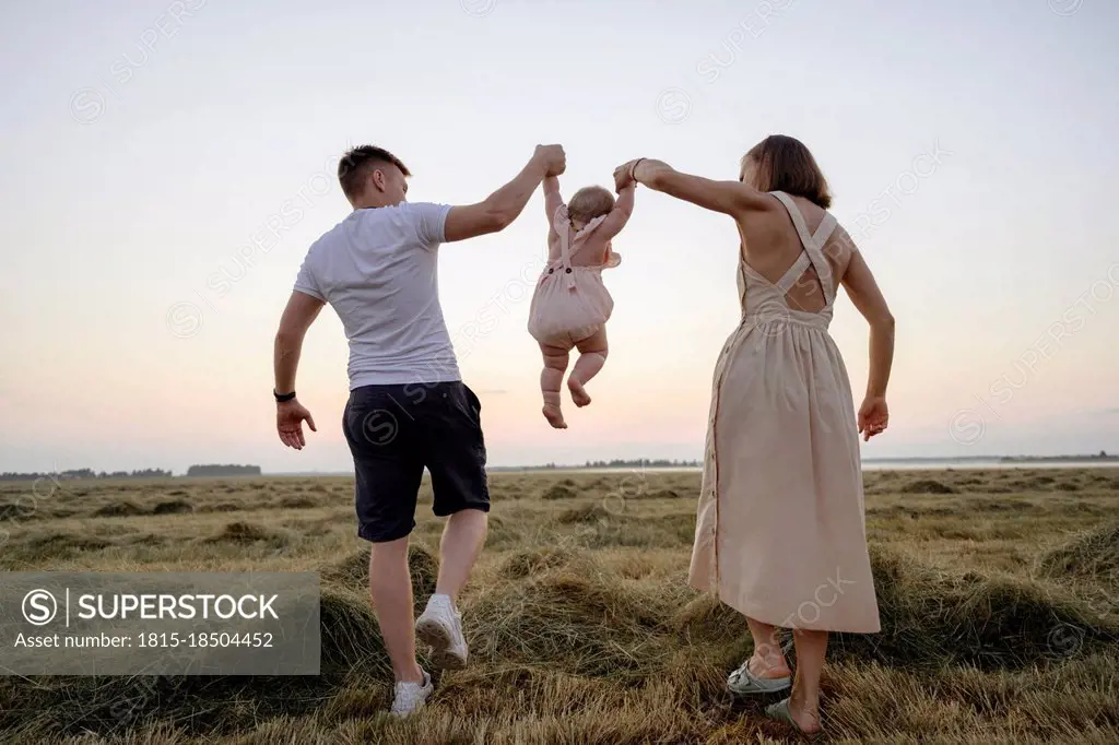 Parents swinging daughter while walking on field