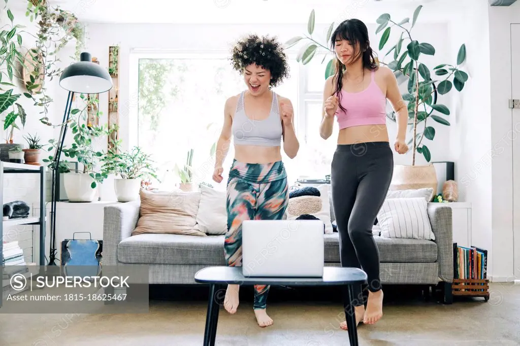 Cheerful friends learning exercise through online tutorial on laptop at home