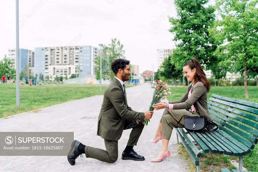 Businessman giving bouquet to colleague while kneeling on footpath