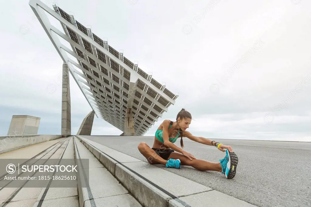 Female athlete stretching legs while sitting on footpath