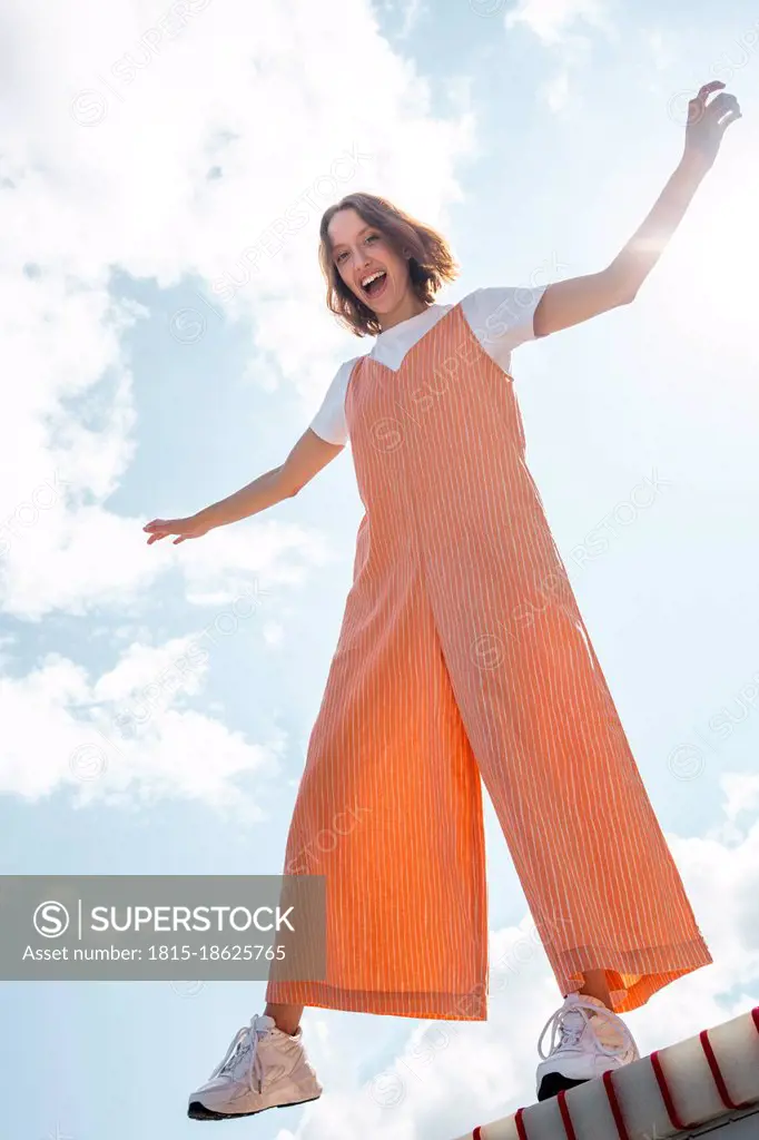 Carefree woman with arms outstretched standing on seesaw during sunny day