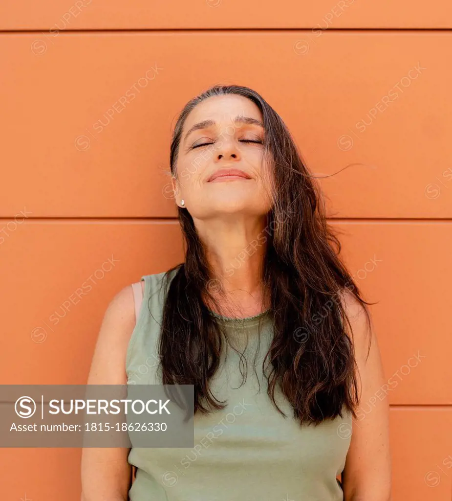 Woman with eyes closed leaning on orange wall