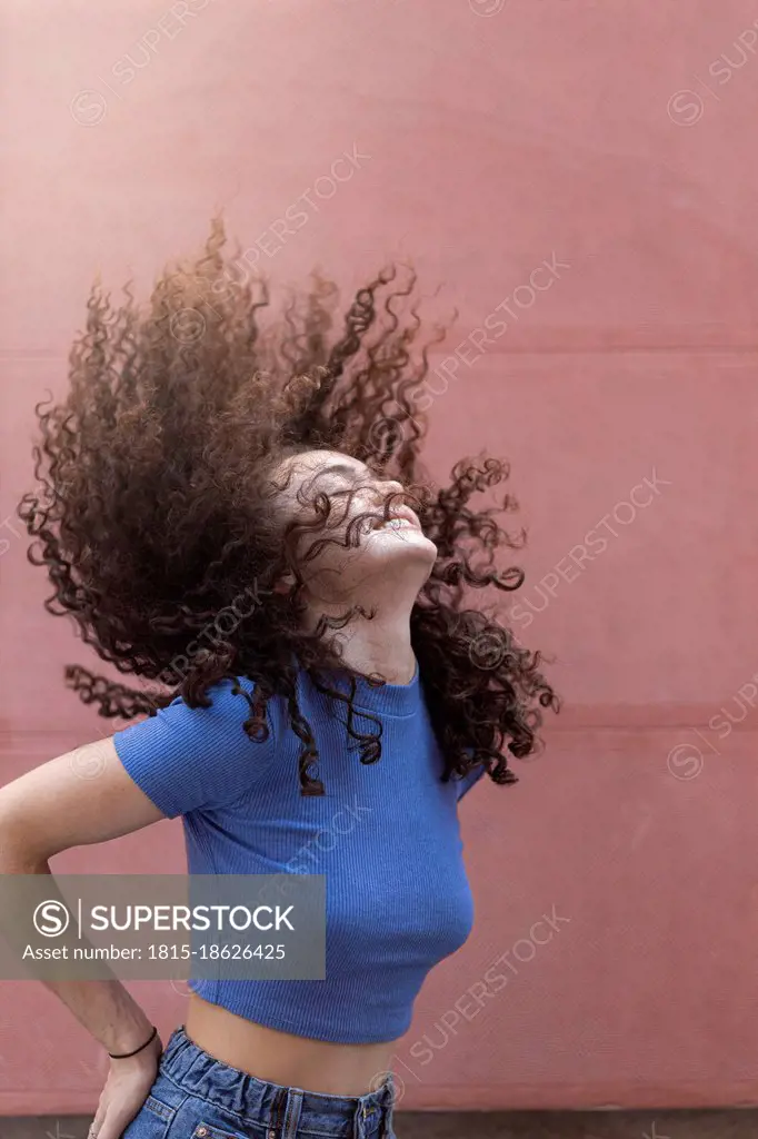 Young woman tossing hair in front of wall