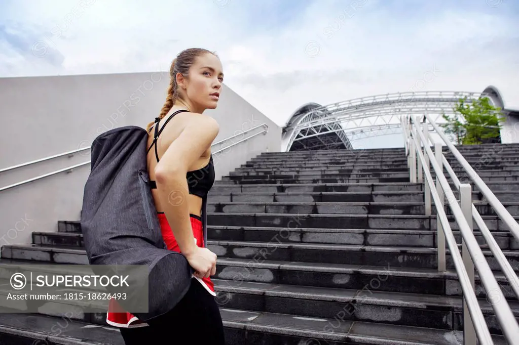 Female athlete with bag standing on steps