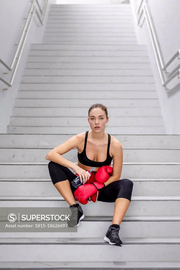 Confident young female athlete sitting on staircase at basement