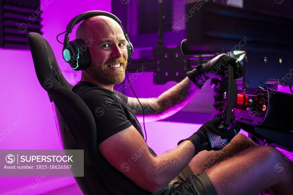 Smiling bald male gamer wearing headphones playing game at studio