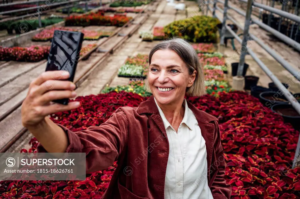 Smiling female farmer taking selfie through smart phone in plant nursery