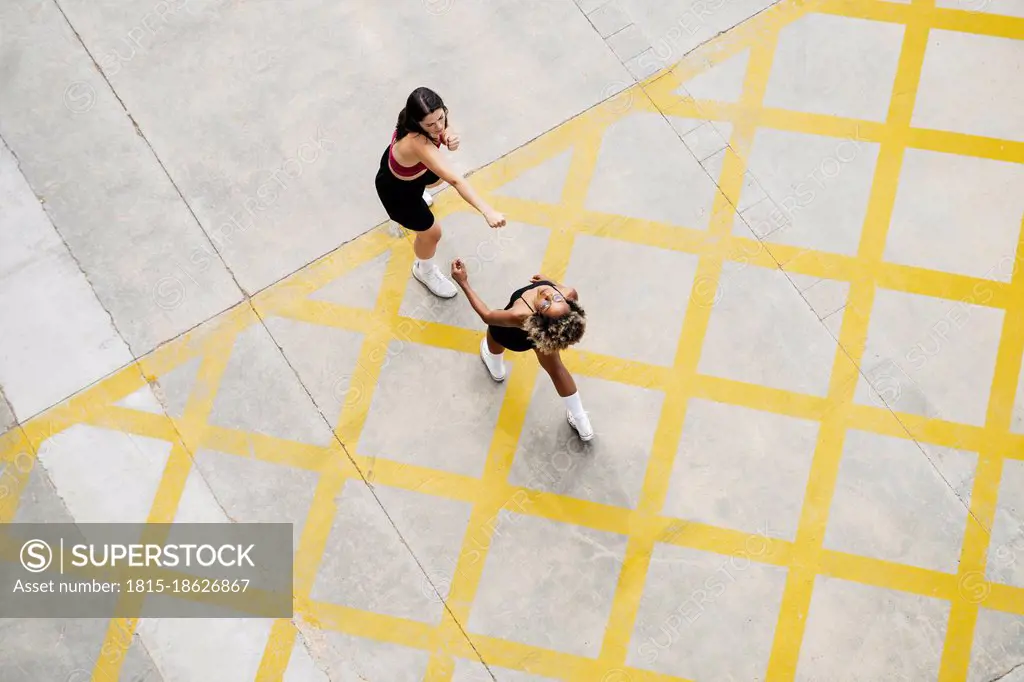 Multi-ethnic female friends boxing on yellow patterned footpath