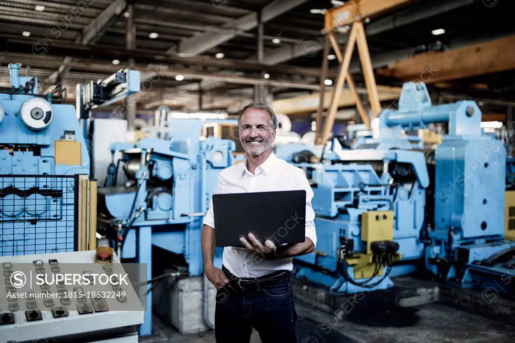 Smiling male professional holding laptop at steel mil