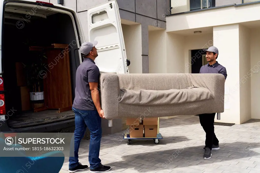 Male delivery coworkers unloading sofa from moving van near house