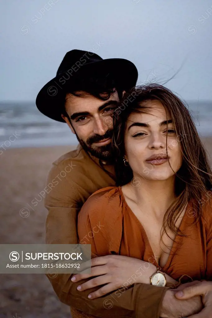 Boyfriend embracing girlfriend from behind at beach during sunset