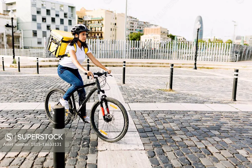 Female delivery person riding bicycle on road in city
