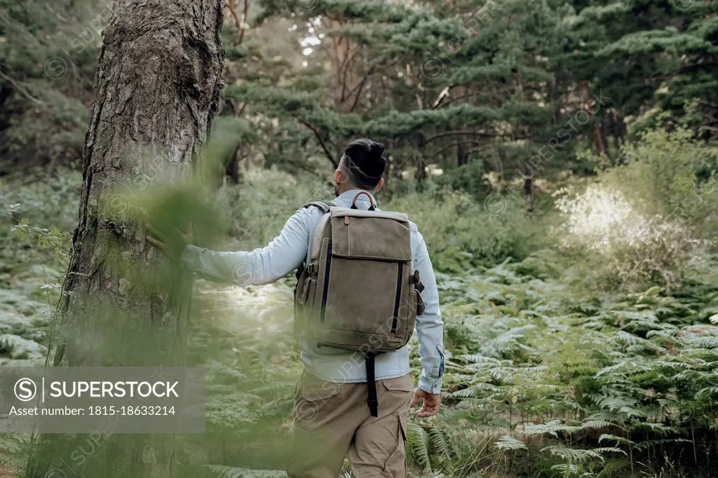 Male backpacker standing by tree in forest