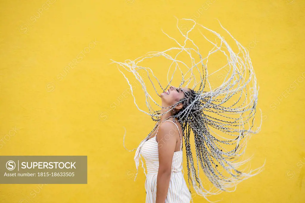 Young woman tossing hair by yellow wall