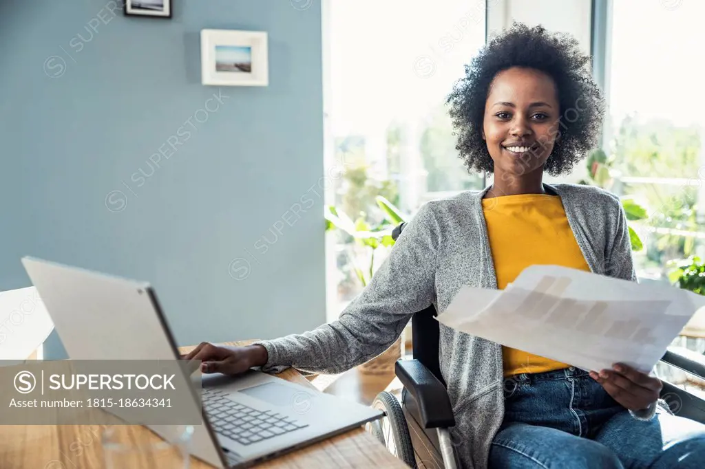 Businesswoman with document sitting on wheelchair in home office