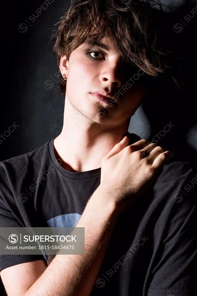 Male teenager touching shoulder against black background
