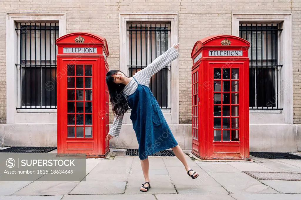 Woman with arms outstretched balancing in front of telephone booth