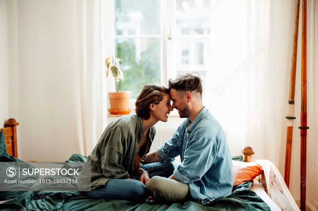 Couple touching foreheads while sitting on bed at home