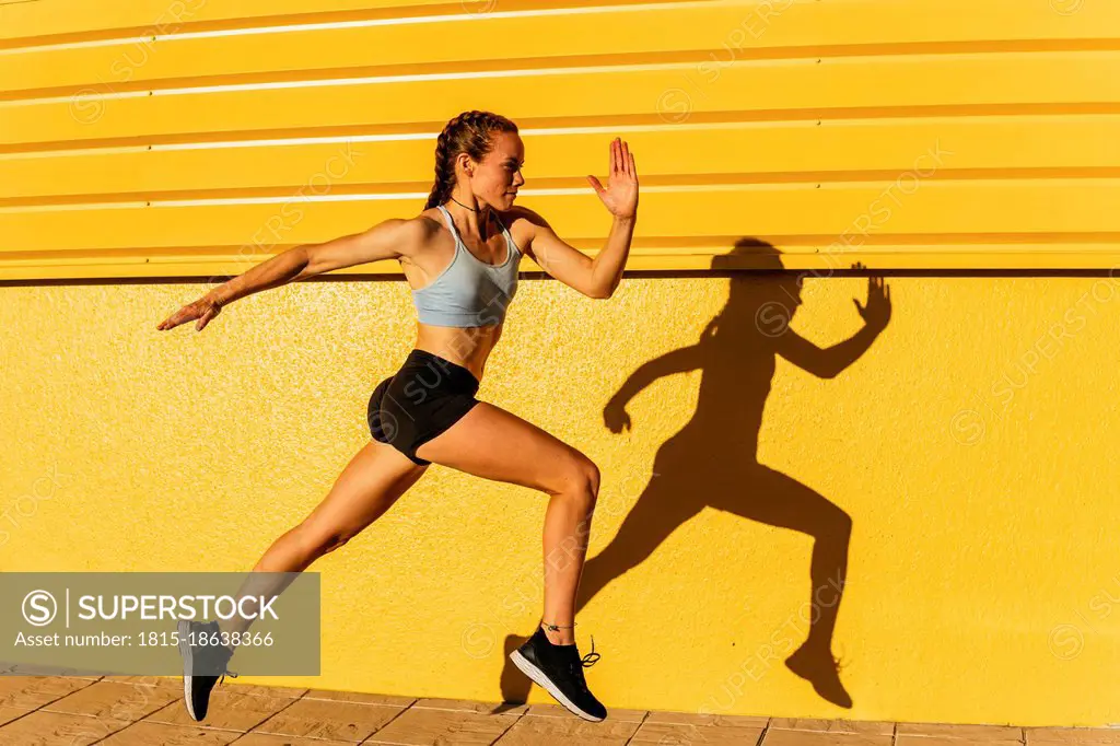 Young female athlete running by yellow wall