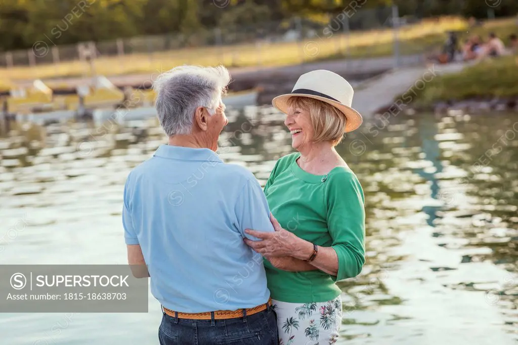 Cheerful senior couple looking at each other while standing by lake