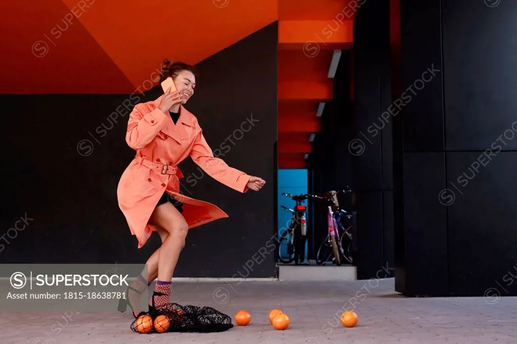 Smiling woman talking on mobile phone by fallen fruit bag