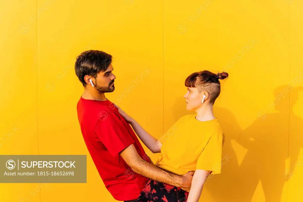 Couple looking at each other while standing by yellow wall