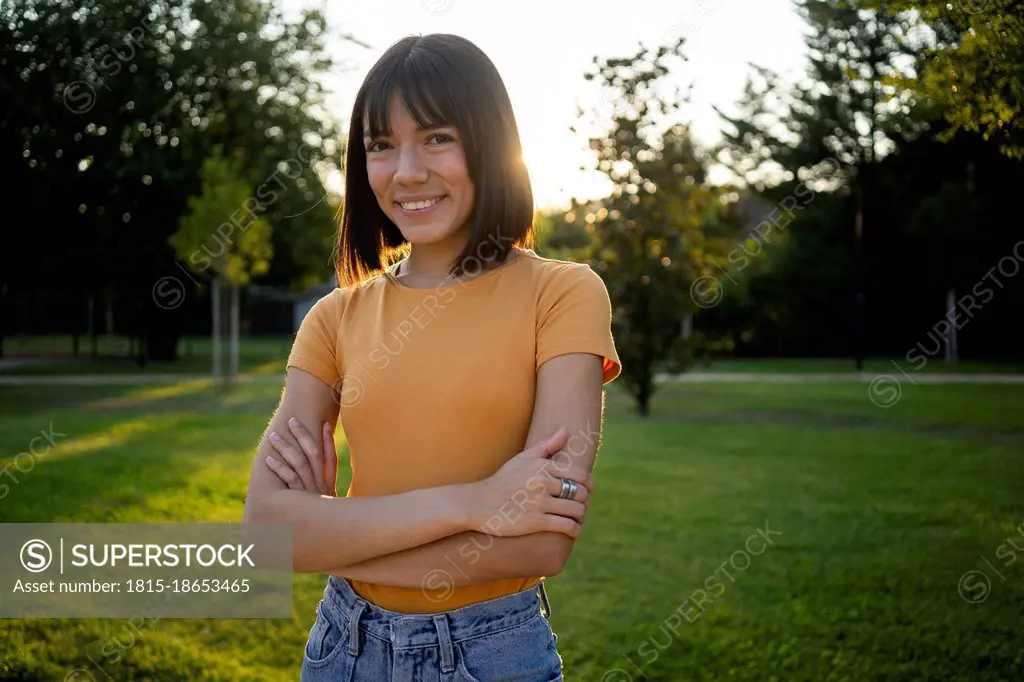 Smiling young woman standing with arms crossed at lawn