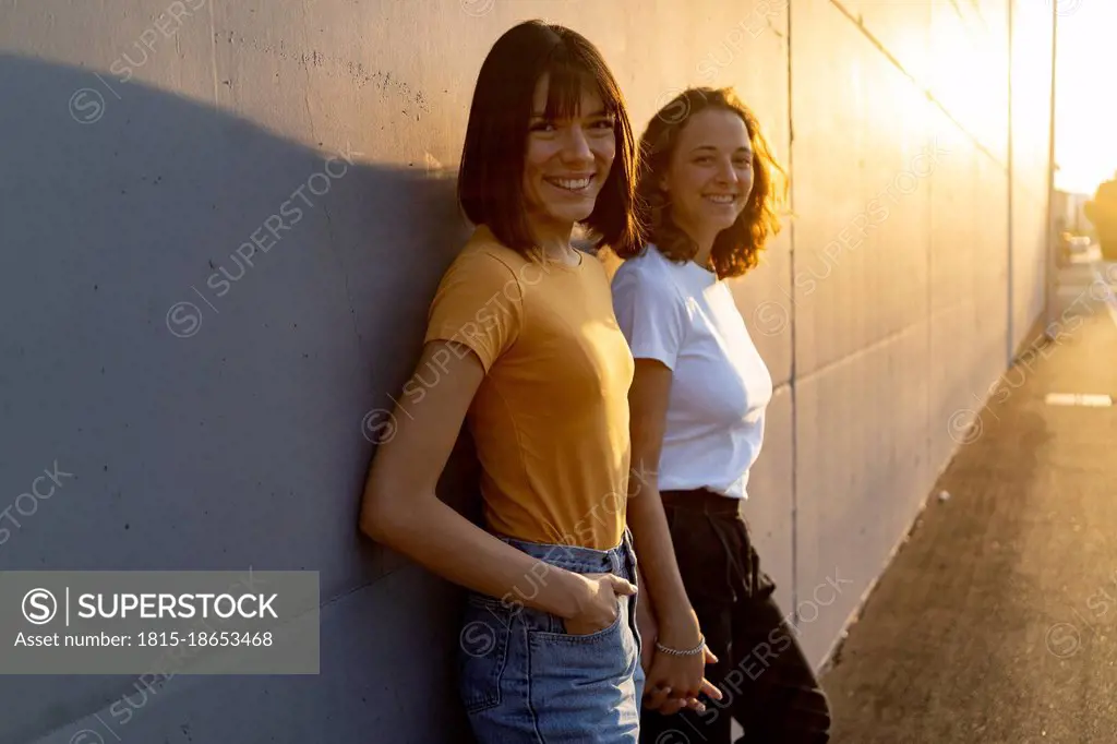 Smiling woman holding hand of girlfriend while leaning on wall